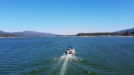 aerial view following rental boat on big bear lake in the san bernardino national forest of california with blue sky and mountains in the background