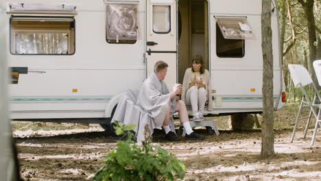 happy couple talking and drinking hot coffee at the camping in the forest