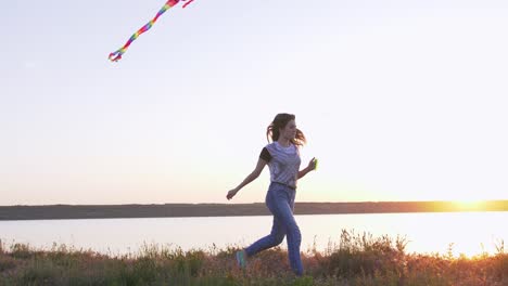 young happy woman and het little dog running with flying kite on a glade at sunset, slow motion