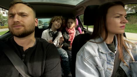 disparado desde el interior de un coche en movimiento: mujer conduciendo como un hombre feliz con sentado en el asiento del pasajero charlando con una niña y un niño sentados en la parte trasera