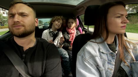 shot from inside of moving car: woman driving as happy man with sitting in passenger seat chatting with little girl and boy sitting in back