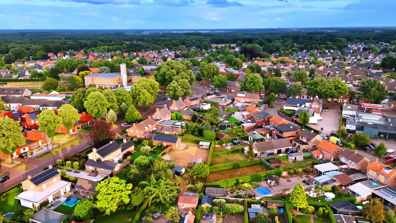 Dronebilde av et landsbysentrum med en moderne kirkebygning. Oversiktsbilde fra luften av bysentrum som viser en moderne kirke, bolighager, solcellepaneler og frodige grønne trær.