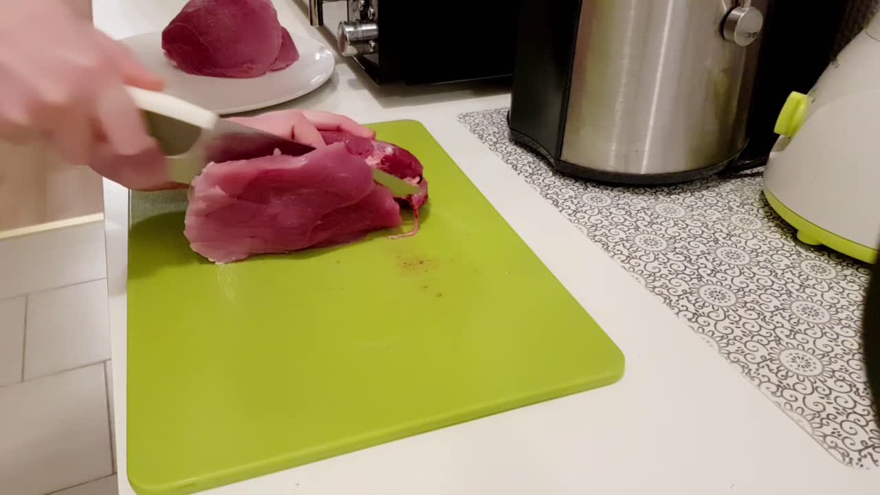 Donna caucasica che taglia carne di maiale con un coltello bianco su un tagliere verde