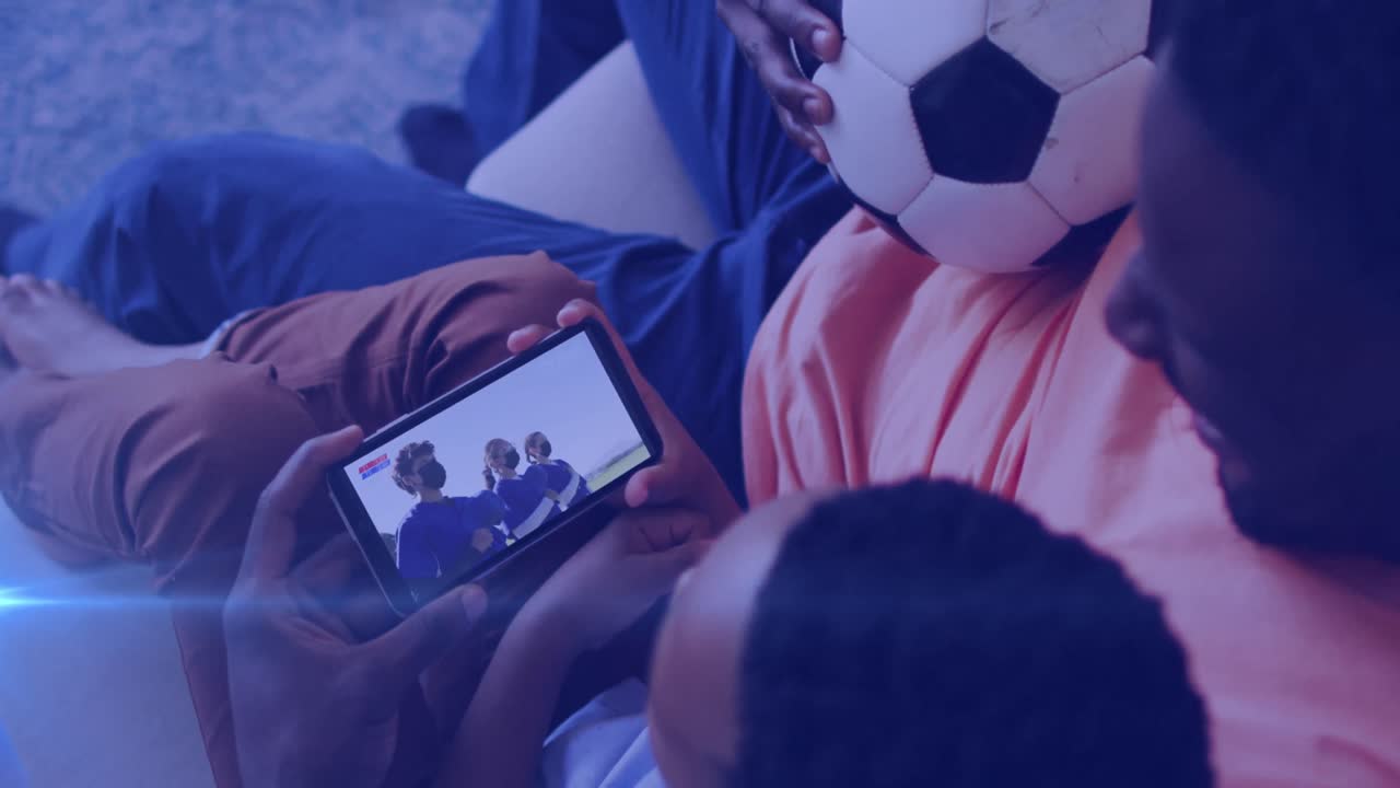 animación de luces brillantes sobre un hombre afroamericano con un hijo viendo fútbol en un teléfono inteligente