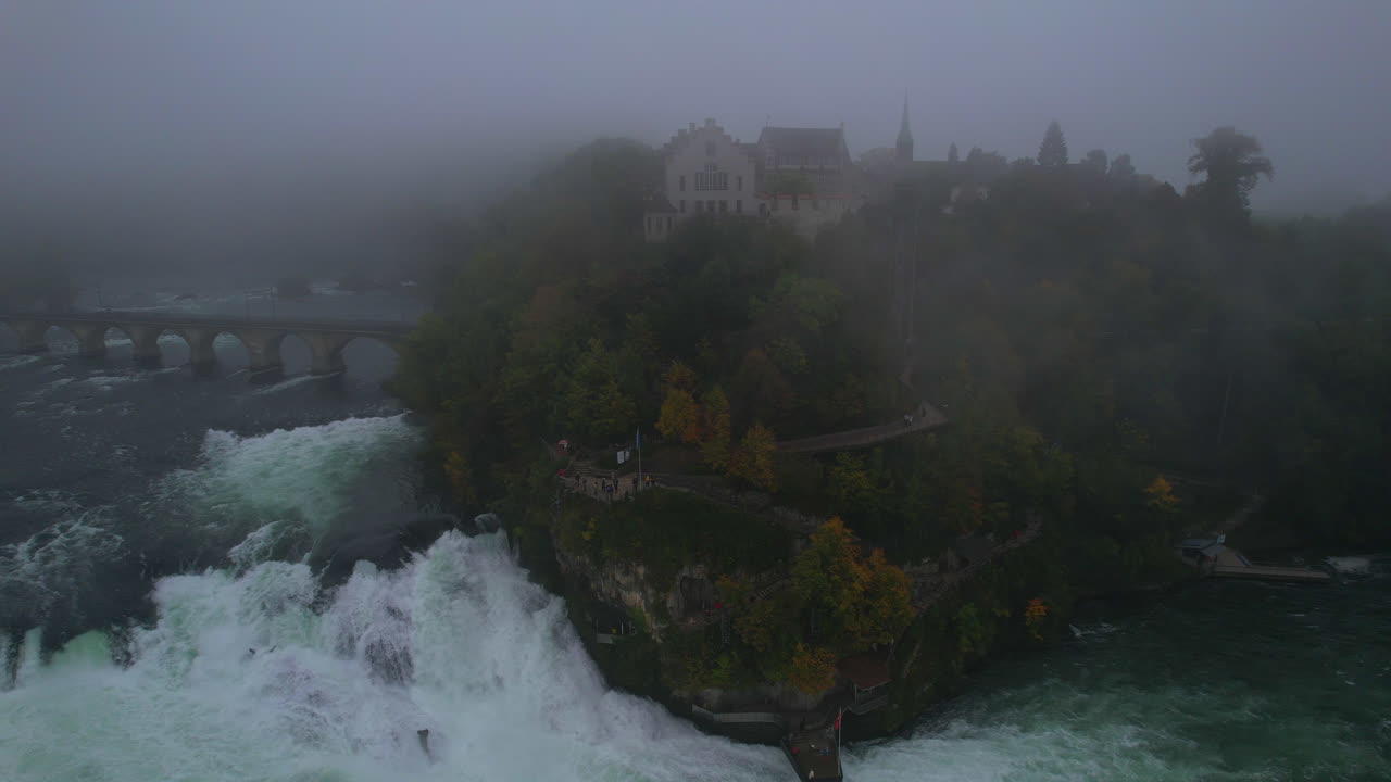 Misty aerial panorama capturing Laufen Castle perched near cascading Rhine Falls, enveloped by atmospheric fog and dramatic landscape in Schaffhausen, Switzerland