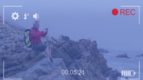 smartphone video interface screen over caucasian senior man sitting on coast filming sea view