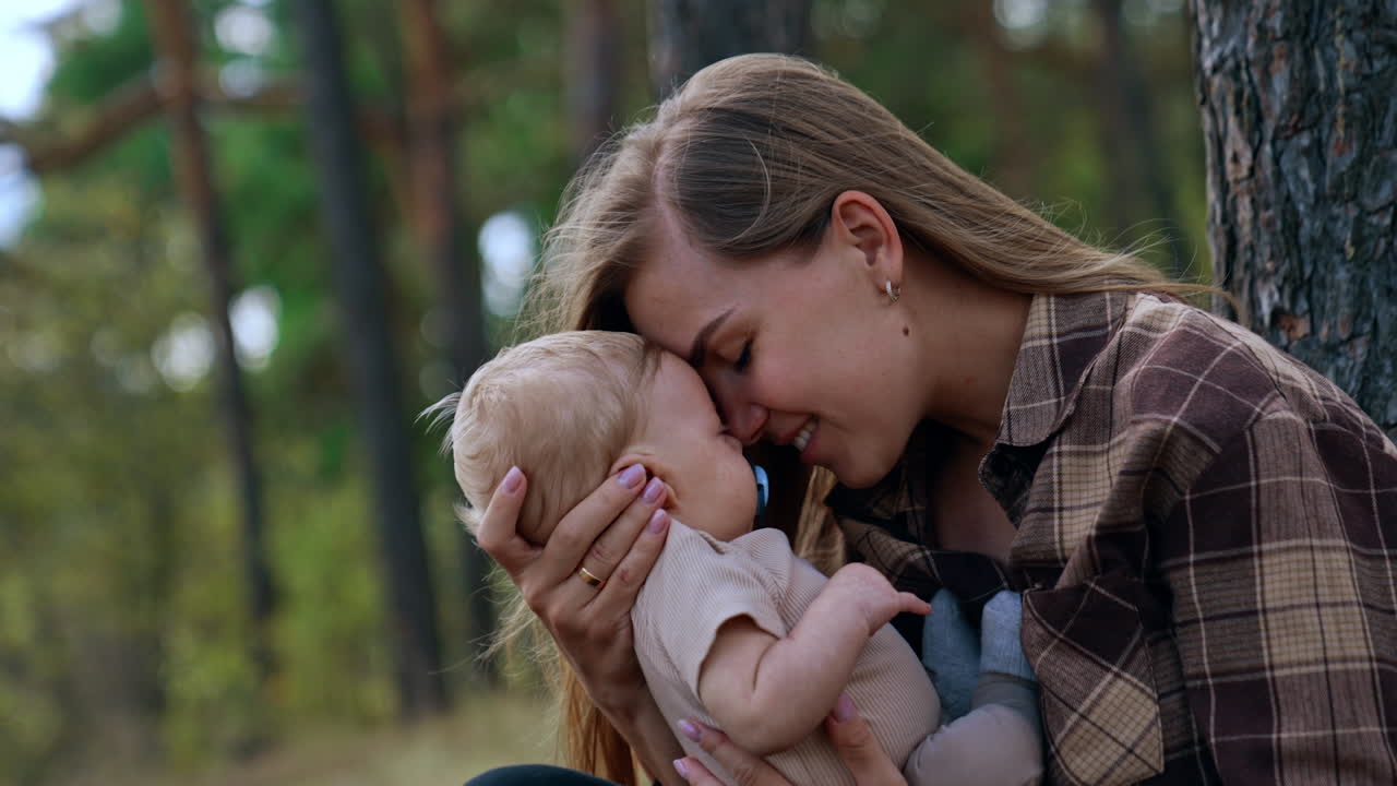 Loving mother leaning to her baby. Mom and son time spent in the nature. Side view.