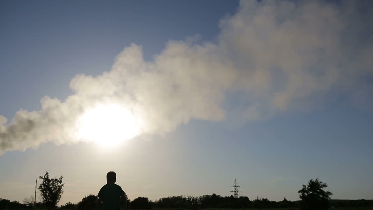 Child Playing With Airplane. Small boy playing with paper airplane at sunset near smoky pipes