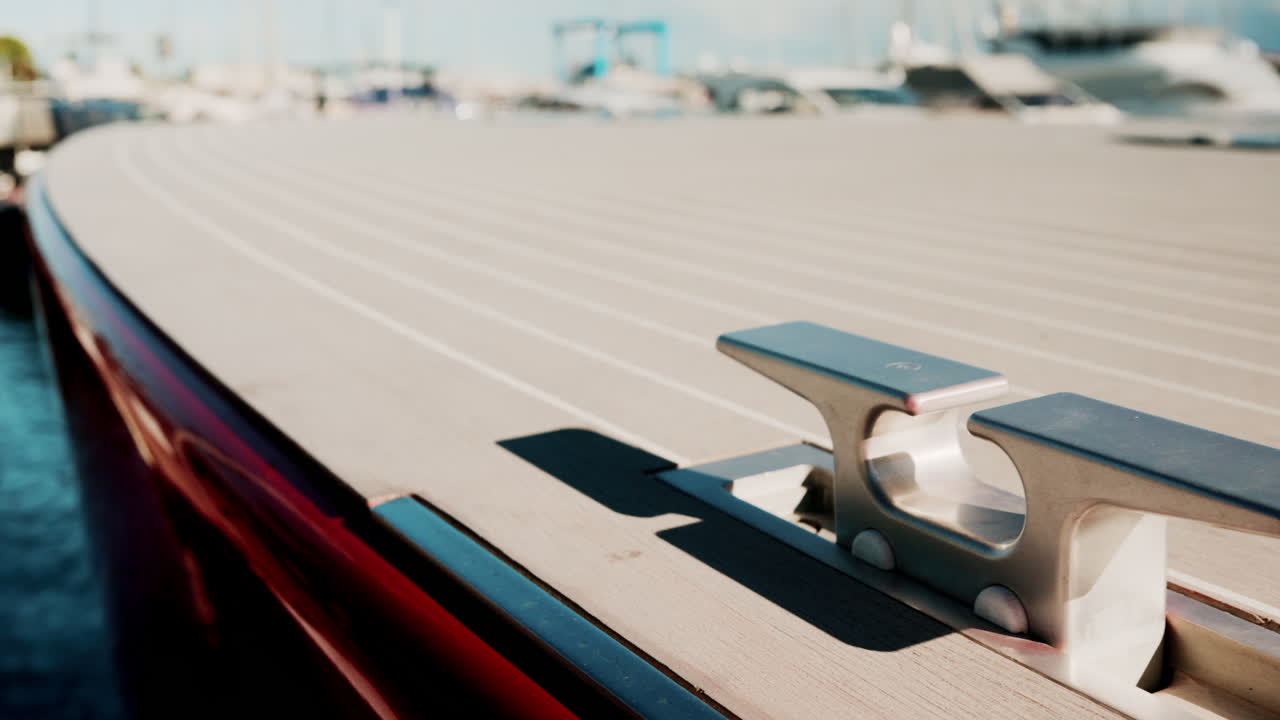 Close up of a sleek red luxury boat deck with metallic cleat, shot in bright sunlight at a marina