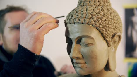 bearded man working on buddha statue hair using a special tool at workshop