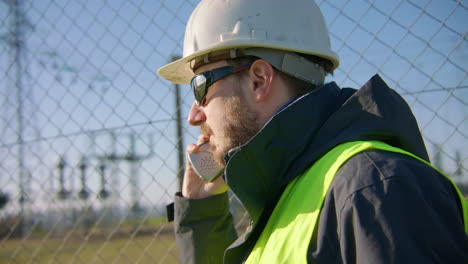 Männlicher-Ingenieur,-Der-über-Das-Radio-Hört-Und-Dabei-Mit-Dem-Kopf-Zum-Umspannwerk-Nickt,-Handheld-Nahaufnahme