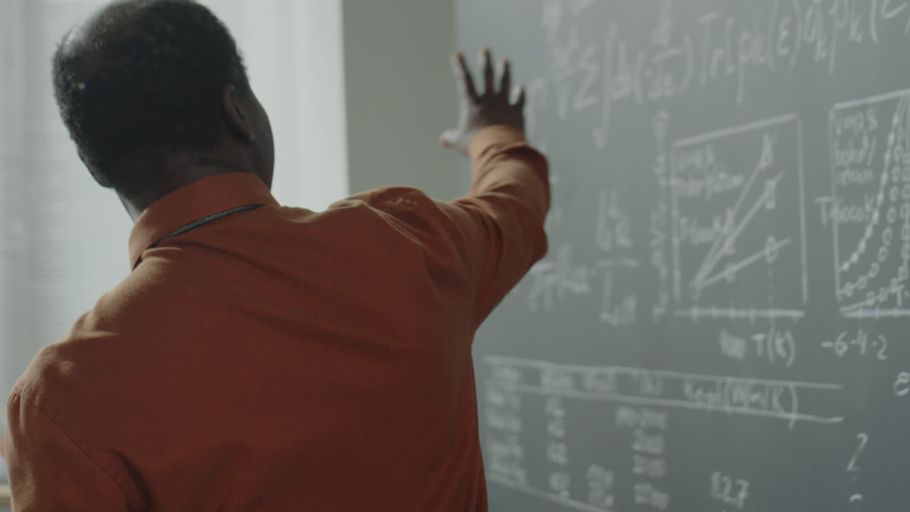 A professor lectures and writes scientific formulas on a blackboard