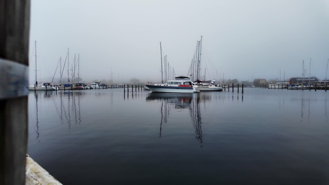 In slow motion, yachts are moored to a wooden pier on a foggy day. Denmark Europe.