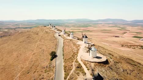 Aerial view of the iconic Molinos de Viento de Consuegra, Spain, perched along a ridge overlooking expansive fields and scenic countryside, highlighting their historic and cultural significance