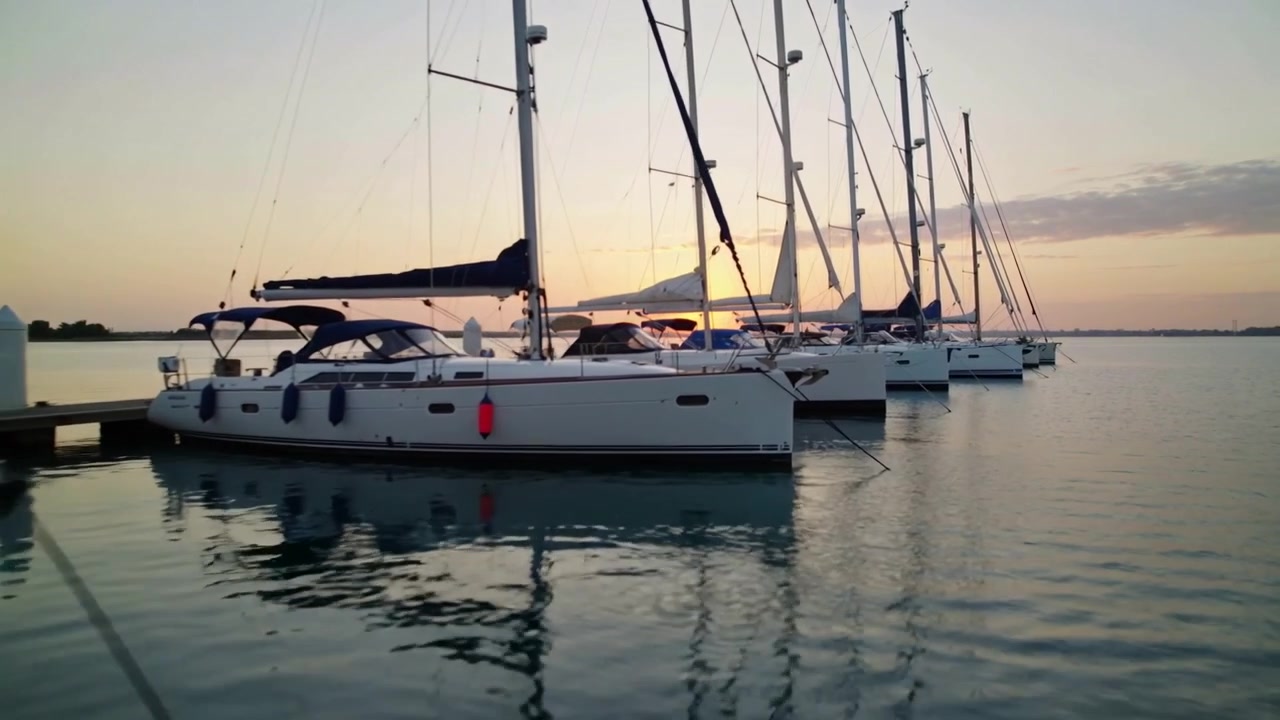 Telecamera in panoramica che rivela una fila di catamarani bianchi ormeggiati al tramonto, catturando i riflessi dei parabordi rossi.