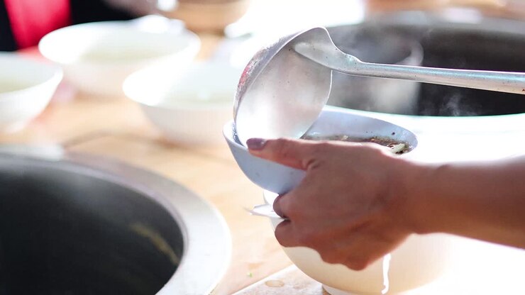 Pouring broth into bowls with noodles