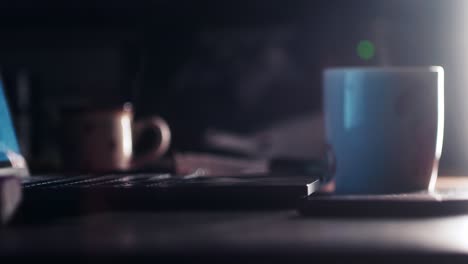 a steaming cup of night tea or coffee by an open computer and lamp light