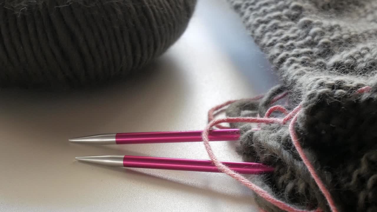 light camera movement to a dark coloured wool - knitting needle stand out of a knitted piece of textile