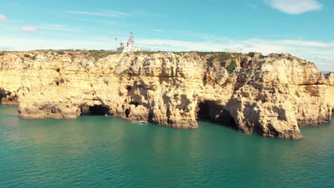 distant view of the lighthouse ponta da piedade overlooking the cliffs and calm sea water, lagos, portugal