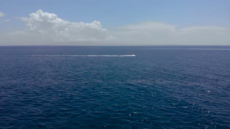 sea jet tracing through deep blue sea water with white clouds and bright sky background