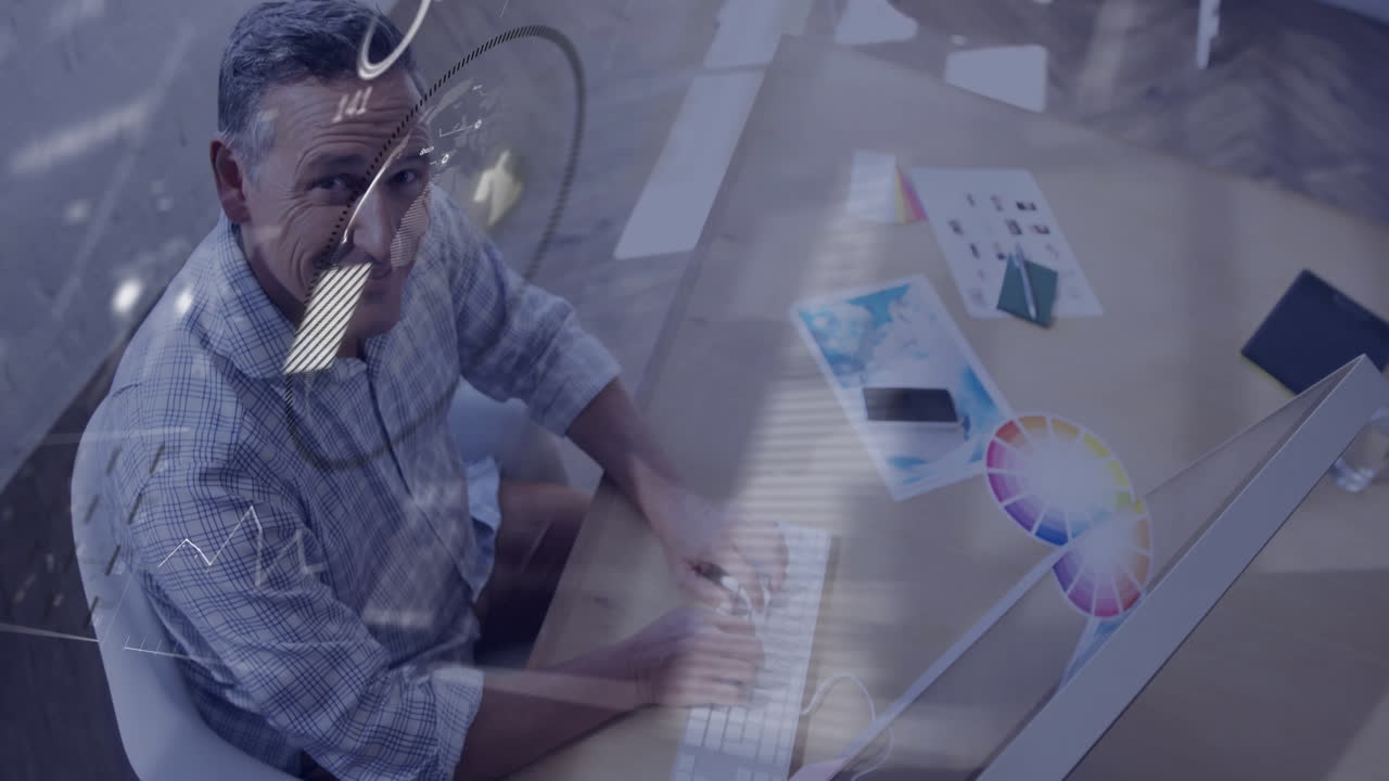 Mature man typing on keyboard at desk in design studio, showing floating graphs charts color wheel