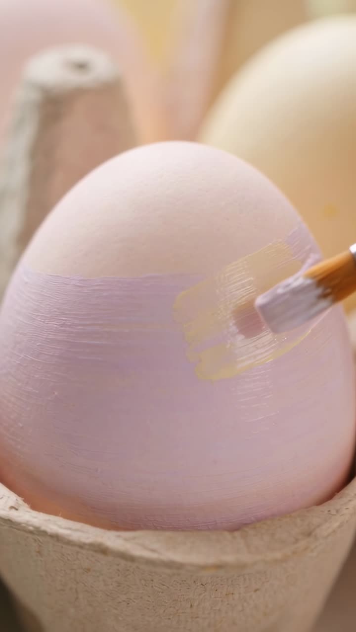 Pale egg sitting in carton, brush approaching right painting lavender band for craft decor