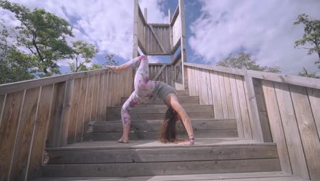 beautiful young woman, performing wheel pose on single leg, outdoors