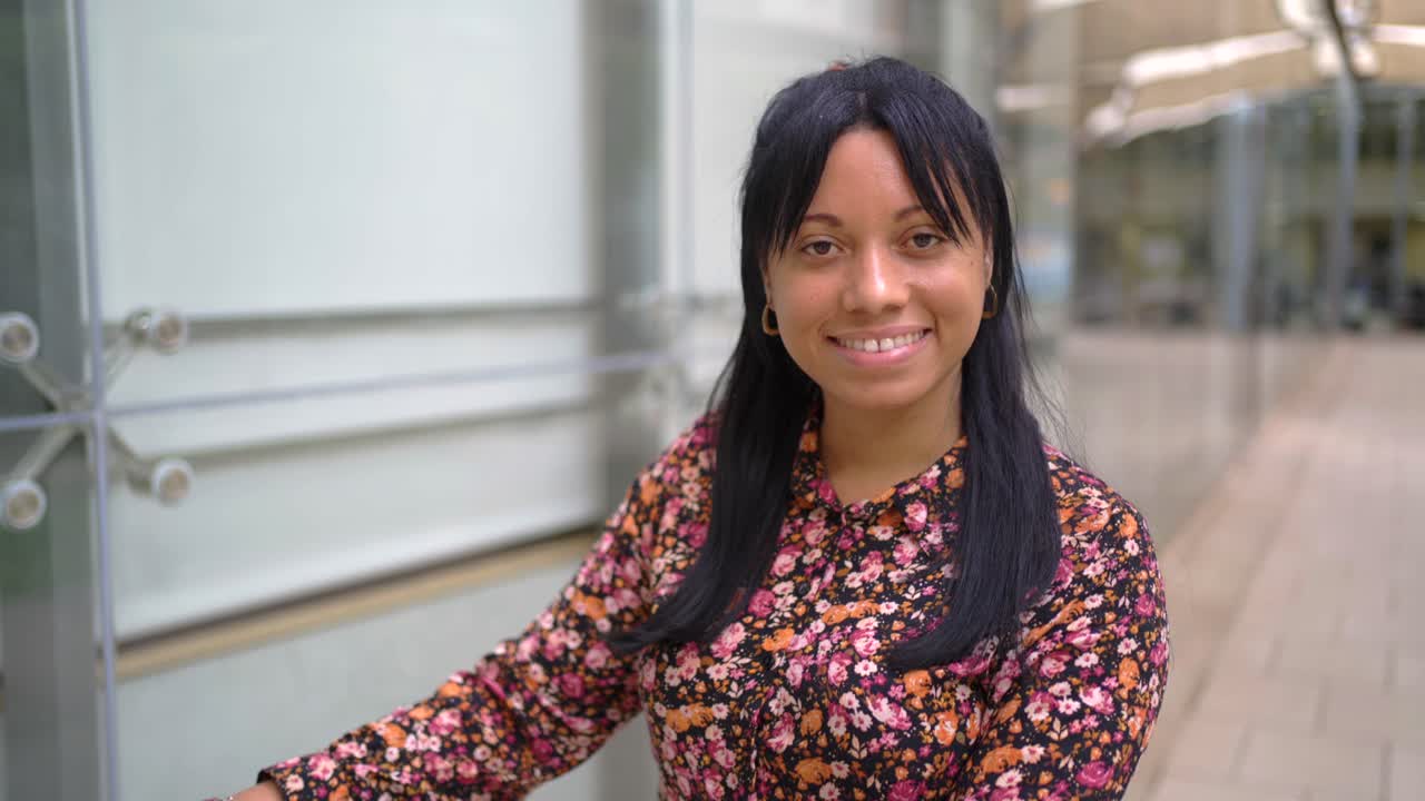mujer étnica sonriente montando un scooter eléctrico en un edificio de oficinas