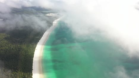 vol aérien dans des nuages bas au-dessus d'une plage de sable tropicale tranquille à l'aube