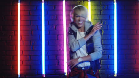 Happy-Woman-In-White-Headphones-Dancing-And-Listening-To-Music-In-A-Room-With-Colorful-Neon-Lamps-On-The-Wall