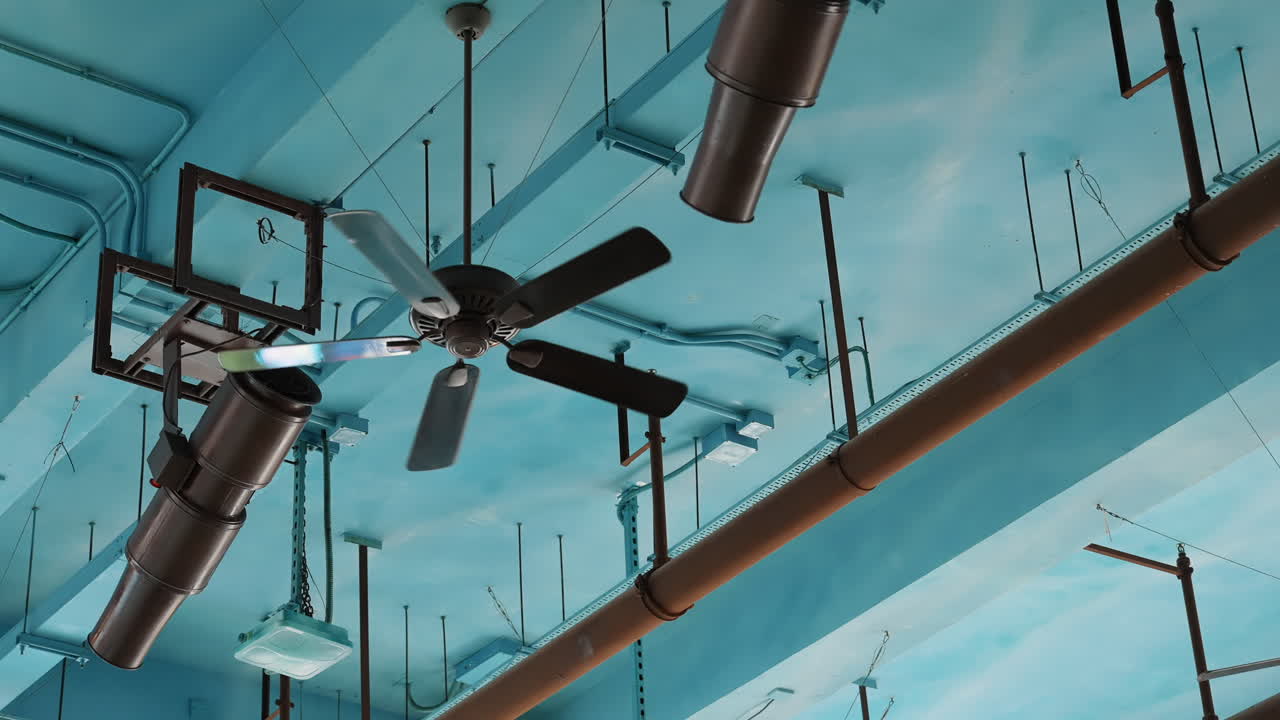 Ceiling fans and pipes against a light blue industrial ceiling