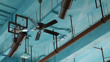 ceiling fans and pipes against a light blue industrial ceiling