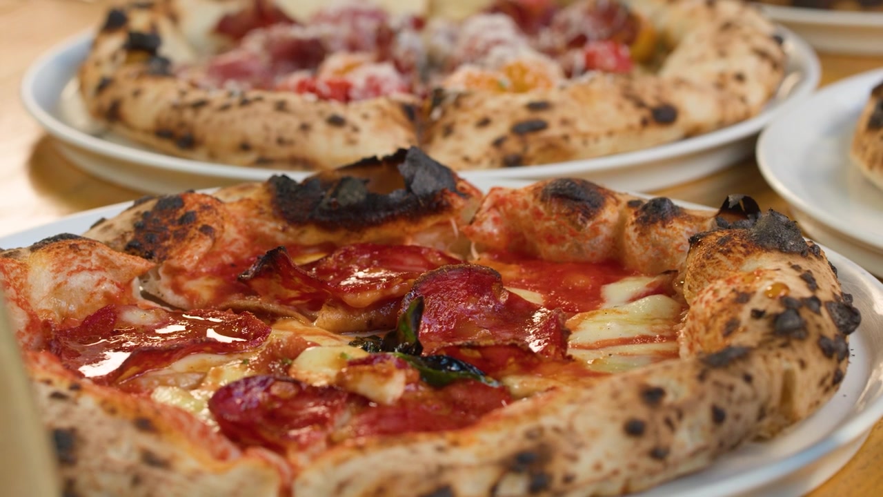 Primo piano di diverse pizze cotte nel forno a legna con bordi bruciacchiati, servite su un tavolo di ristorante