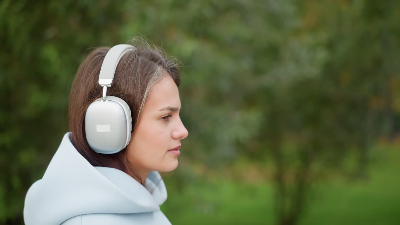 Close-up view of pretty lady in headphones listening to music in garden with blurred trees background, perfect for scenes depicting relaxation, outdoor activities, or enjoying nature with music