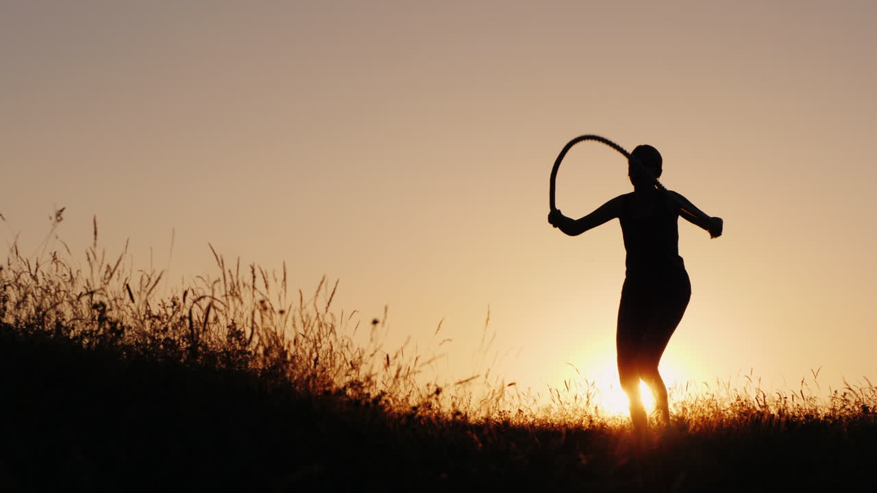 Training In The Fresh Air - A Silhouette Of A Woman Jumping Over A Rope At Sunset