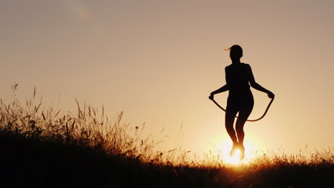 Training-An-Der-Frischen-Luft---Eine-Silhouette-Einer-Frau,-Die-Bei-Sonnenuntergang-über-Ein-Seil-Springt