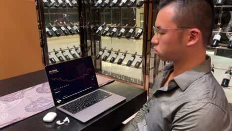 wealthy asian male experiencing stress and frustration over stock market loss on laptop in luxury setting