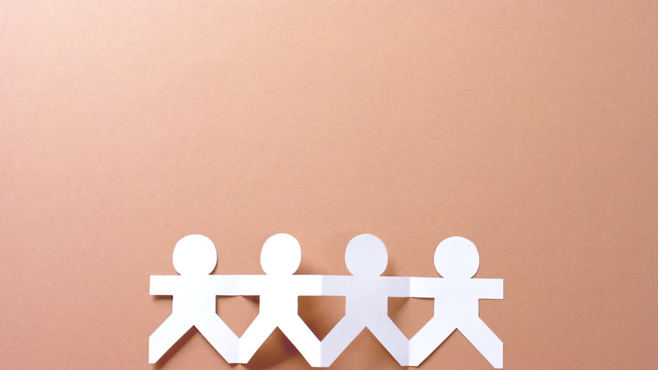 Close up of people holding hands made of white paper on beige background with copy space