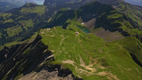 aerial view of a mountain range in summer with green grass, peaks and slopes and a little pond, with a lake and mountains in the background