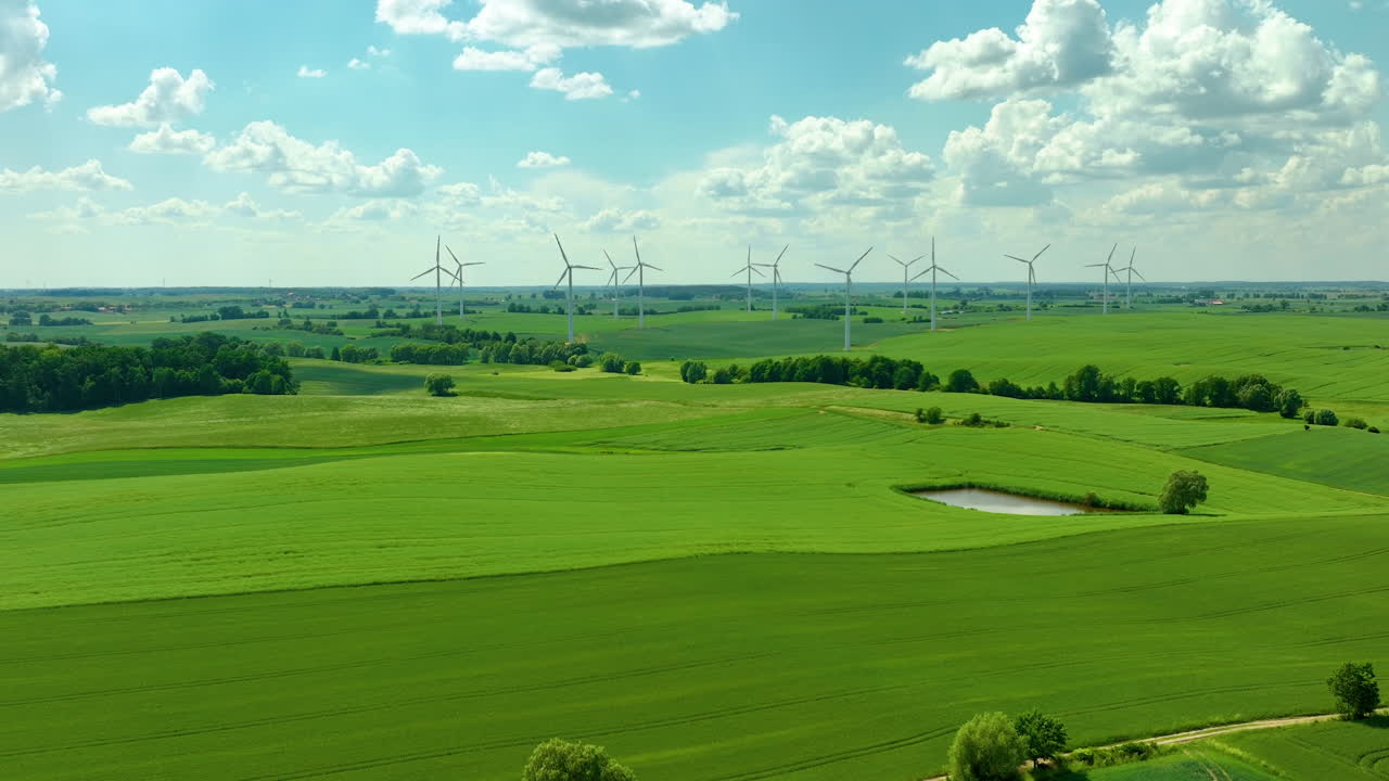 Aerial a wind farm in a rural area with wind turbines scattered across green fields, a bright blue sky with fluffy clouds