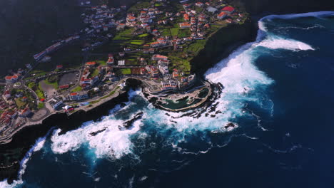 descending aerial view of porto moniz with natural pool and crashing waves against coastline during sunny day