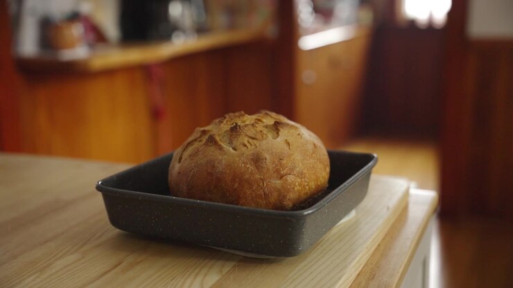A baker at home places a hot fresh baked loaf of bread in a tray onto a counter top to cool.
