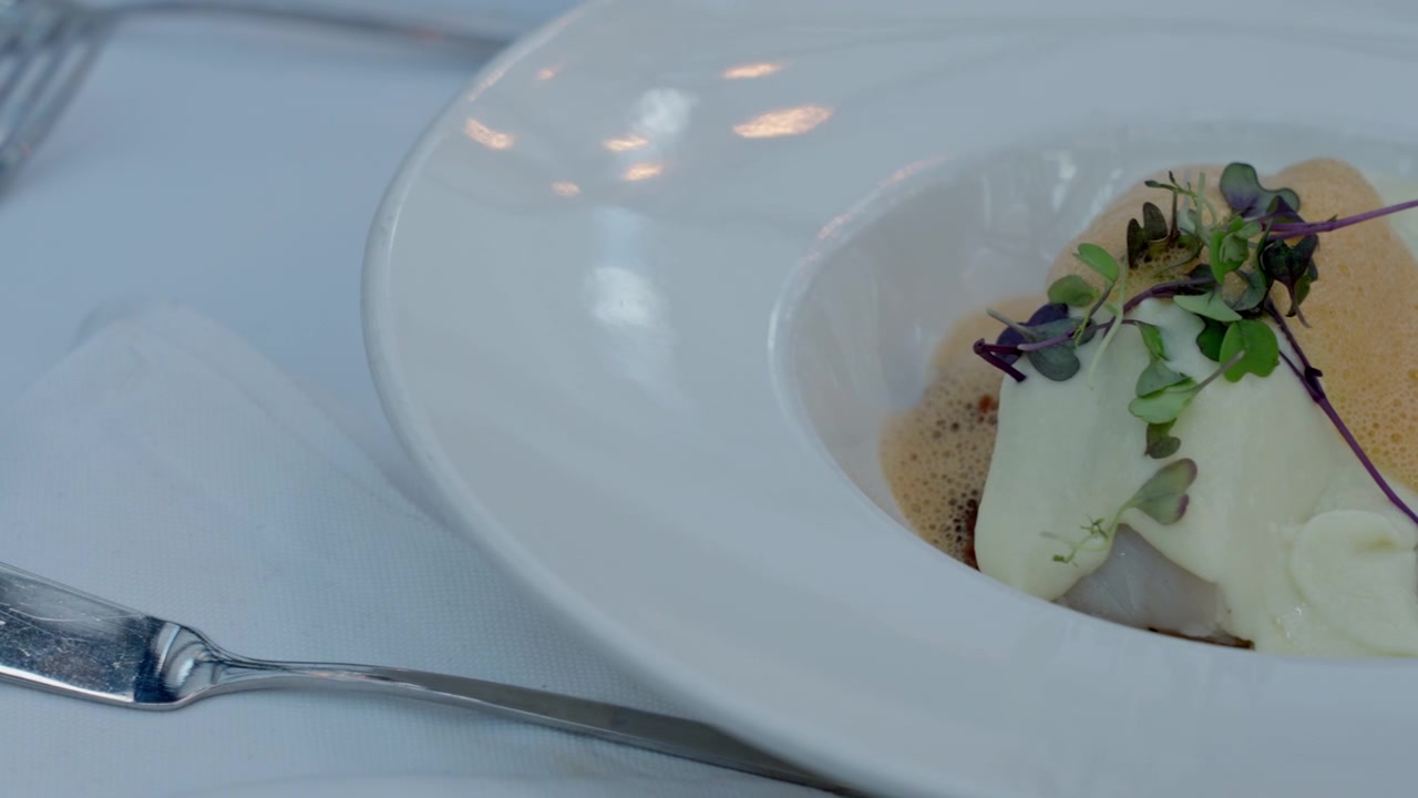 Gastronomisch wit visgerecht geserveerd in een moderne witte kom, met romige topping, microgroenten en delicaat schuim. Fine dining concept.