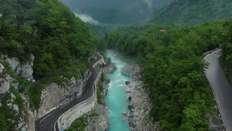 drone-shot-of-the-soca-river-in-slovenia-with-blue-water,-a-steet-on-the-left-site-and-trees-around-on-a-cloudy-day