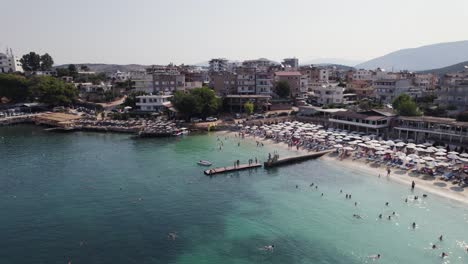 Aerial-View-Of-Busy-Crowded-Plazhi-Ksamil-9-Beach-With-Mini-Dock,-Albania