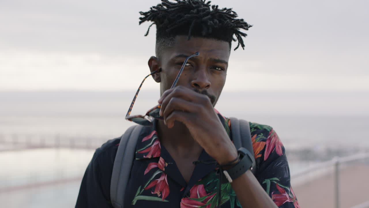retrato de un encantador hombre afroamericano que se quita las gafas de sol sonriendo con confianza junto a la playa de la piscina