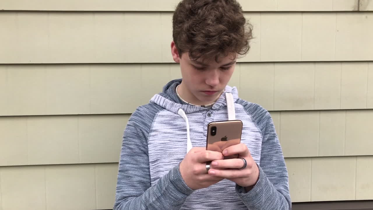 Camera panning from left to right, revealing an teenage boy texting on his new iPhone x