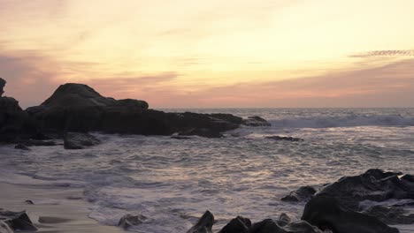 Sunset-on-the-beach,-rough-sea-with-waves-breaking-against-rocks-in-the-sea,-Cadiz,-Spain