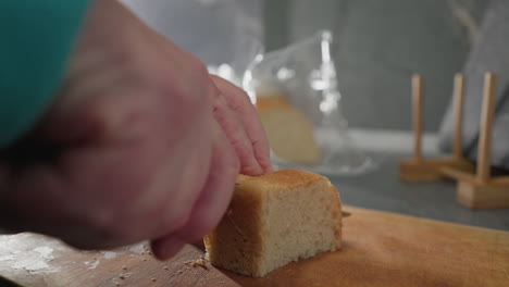 Close-up shot of older woman slicing freshly baked bread with a knife on wooden cutting board in kitchen. Soft lighting, kitchen tools, and bread packaging visible in background