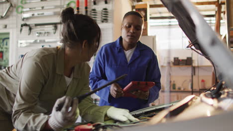 video of two diverse female car mechanics using tablet and repairing car